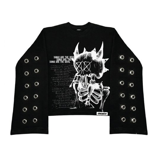 A black long-sleeve crop top sweatshirt featuring a large white graphic of a horned skull and skeleton on the front, with text on the left side. The sleeves are decorated with multiple rows of silver metal grommets, and a small 'Delusion' brand label is visible near the bottom right hem.